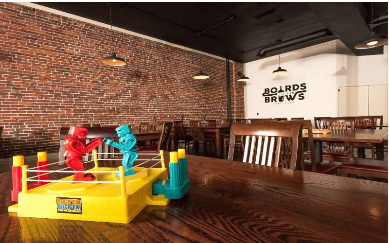 The dining room: Rock 'Em Sock 'Em Robots on a wooden table, pendant lights and the Boards & Brews logo on the wall