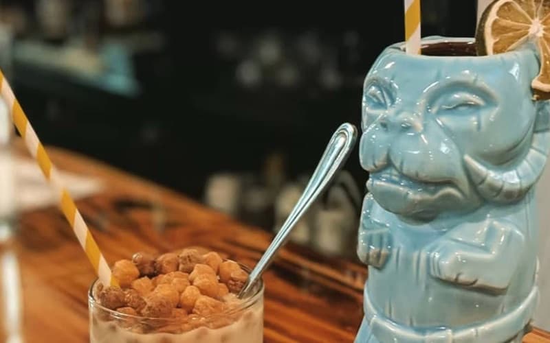 A tiki mug and a cereal-topped drink on the bar