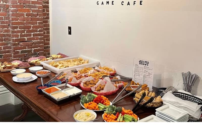 Party platters laid out on a long table: fries, spring rolls, sandwiches, salad and vegetables